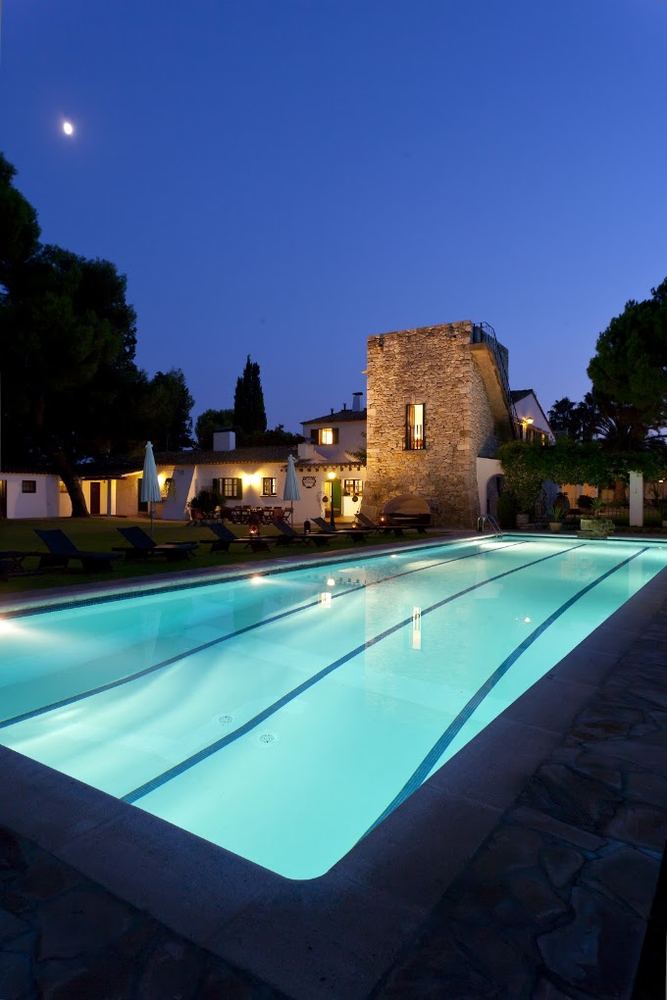 Piscina iluminada de noche junto a la torre de piedra